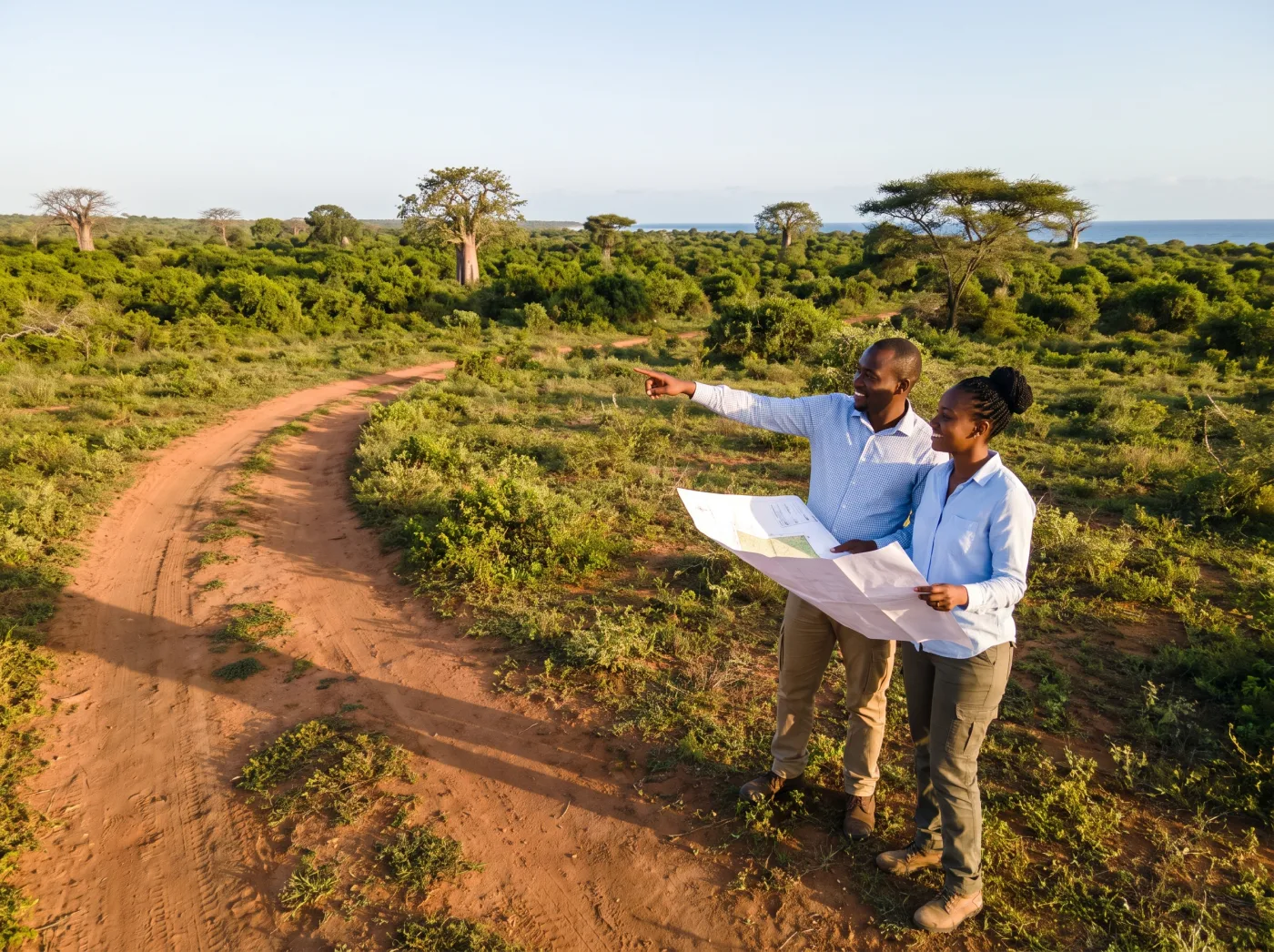 A couple standing on the graded access road at Furaha Gardens, holding the site plan and looking out across the plots